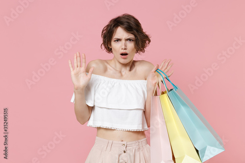 Shocked young woman girl in summer clothes hold package bag with purchases isolated on pink background in studio. Shopping discount sale concept. Mock up copy space. Rising hands up, showing palms.