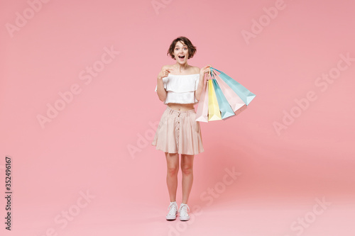 Excited young woman girl in summer clothes isolated on pastel pink wall background studio. Shopping discount sale concept. Mock up copy space. Pointing index finger on hold package bag with purchases.