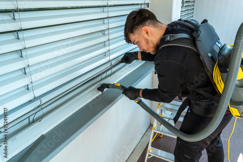 professional cleaner vacuum cleaning window blinds on an apartment balcony © makasana photo