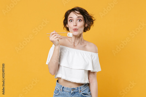 Young brunette woman girl in casual clothes hold in hand sticks chopsticks with makizushi sushi roll traditional japanese food isolated on yellow background studio portrait. People lifestyle concept.