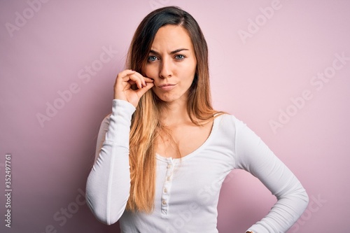 Young beautiful blonde woman with blue eyes wearing white t-shirt over pink background mouth and lips shut as zip with fingers. Secret and silent, taboo talking