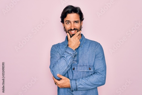 Young handsome hispanic bohemian man wearing hippie style over pink background looking confident at the camera smiling with crossed arms and hand raised on chin. Thinking positive.