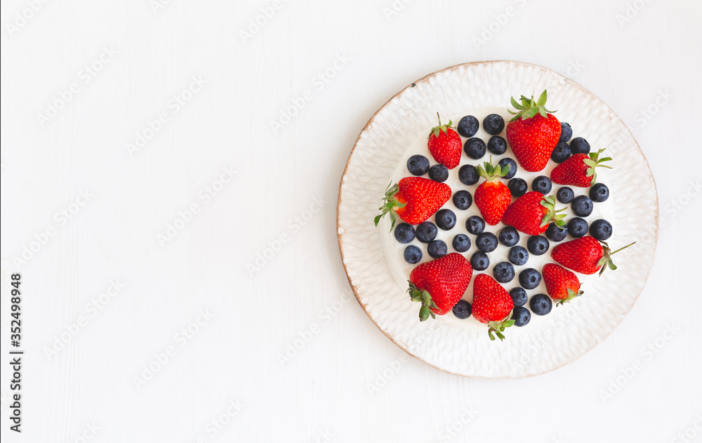 A top view of home made cake or pie on beautiful white handmade plate on light wooden background with copy space. Dessert is decorated with summer berries, strawberries and blueberries A top view of home made cake or pie on beautiful white handmade plate on light wooden background with copy space. Dessert is decorated with summer berries, strawberries and blueberries