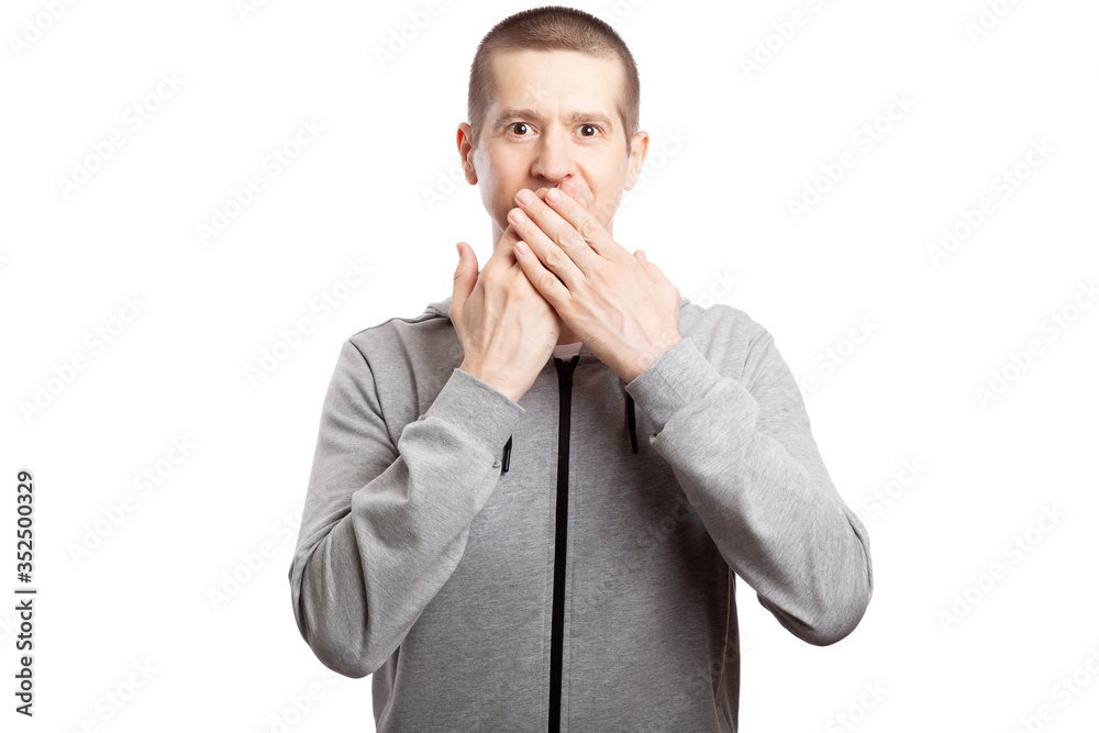 healthy, athletic male athlete shows a gesture of silence and mystery, asks to remain silent, puts his index finger to his lips. Dressed in a grey hooded jacket. A look into the camera. Isolated healthy, athletic male athlete shows a gesture of silence and mystery, asks to remain silent, puts his index finger to his lips. Dressed in a grey hooded jacket. A look into the camera. Isolated