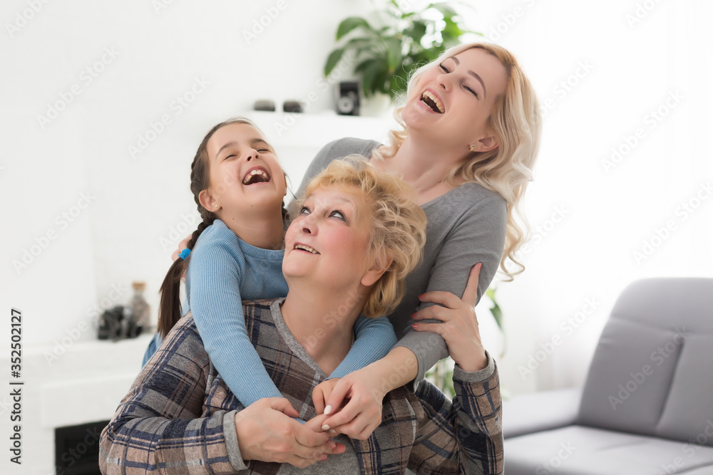 Three generations of women. Beautiful woman and teenage girl are kissing their granny while sitting on couch at home