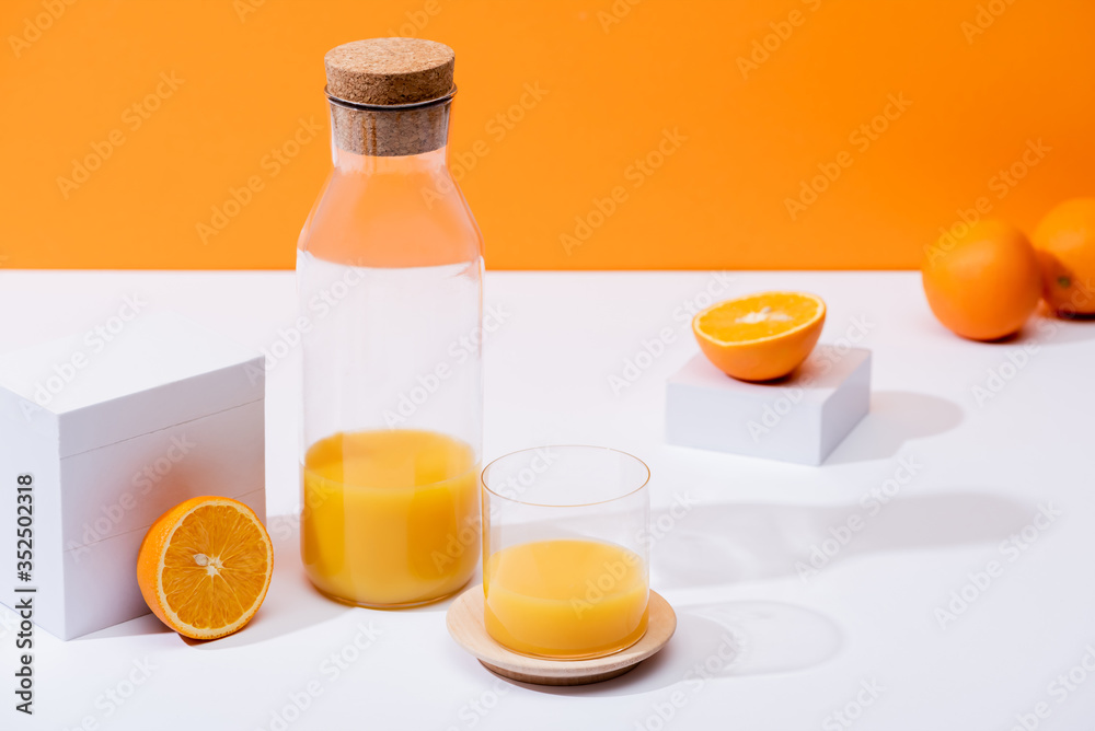 fresh orange juice in glass and bottle near ripe oranges on white surface isolated on orange