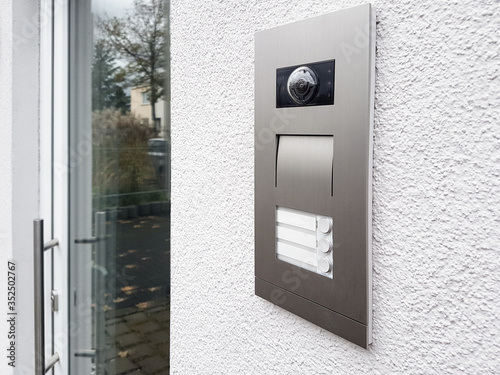 Intercom on white textured wall. Facade house with glass door. Close up