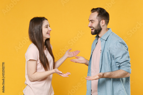 Side view of cheerful young couple two friends guy girl in casual clothes posing isolated on yellow background. People lifestyle concept. Mock up copy space. Looking at each other, speaking talking.