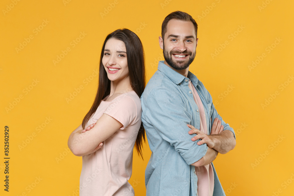 Smiling young couple two friends guy girl in pastel blue casual clothes isolated on yellow wall background. People lifestyle concept. Mock up copy space. Standing back to back, holding hands crossed.