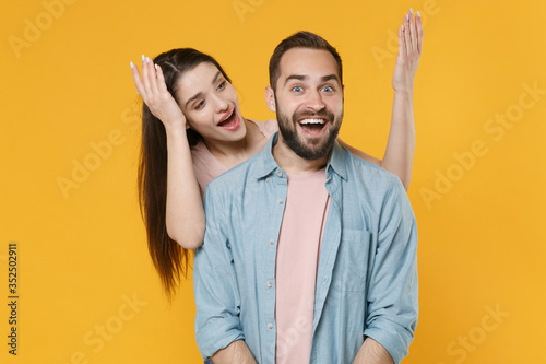 Surprised amazed young couple two friends guy girl in pastel blue casual clothes posing isolated on yellow background studio portrait. People lifestyle concept. Mock up copy space. Spreading hands.