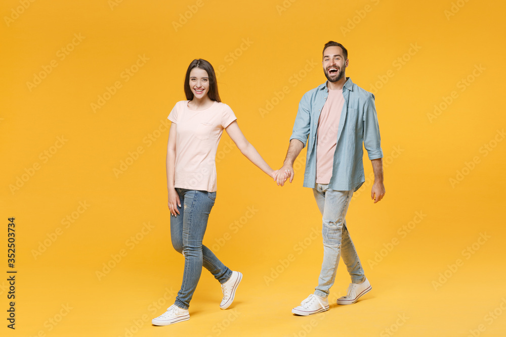 Cheerful young couple two friends guy girl in pastel blue casual clothes posing isolated on yellow background studio portrait. People lifestyle concept. Mock up copy space. Walking, holding hands.