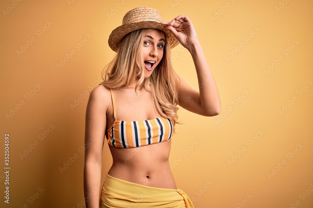Young beautiful blonde woman on vacation wearing bikini and hat over yellow background surprised with hand on head for mistake, remember error. Forgot, bad memory concept. Young beautiful blonde woman on vacation wearing bikini and hat over yellow background surprised with hand on head for mistake, remember error. Forgot, bad memory concept.