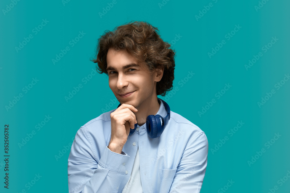 Cunning man. Portrait of a young beautiful man wearing white t-shirt and blue shirt in blue headphones.Thought and holds a fist at the chin and looking at camera Cunning man. Portrait of a young beautiful man wearing white t-shirt and blue shirt in blue headphones.Thought and holds a fist at the chin and looking at camera