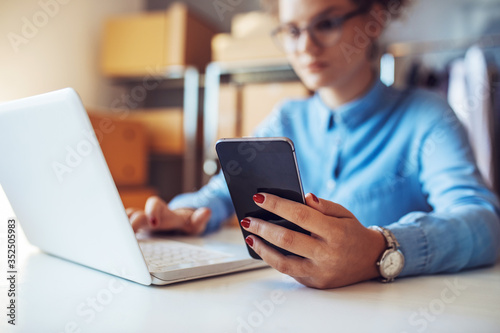 Smiling businesswoman working and using phone in office. Small business entrepreneur looking at her mobile phone and smiling.