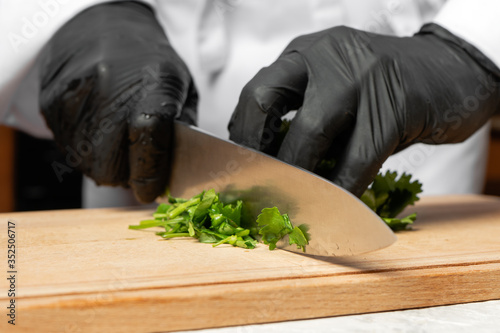A cook in black gloves is cutting parsley.
