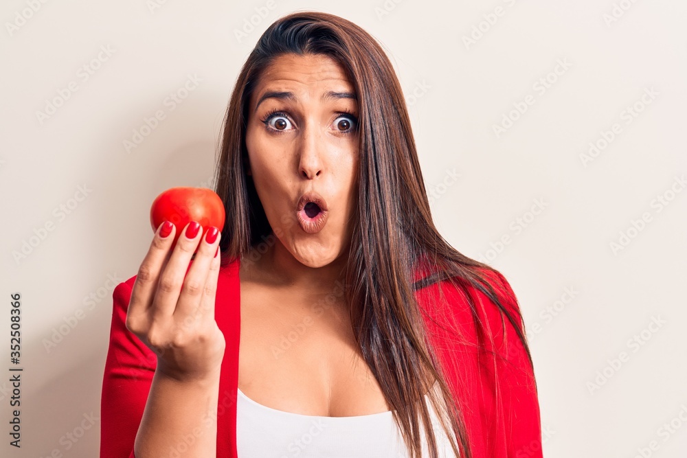 Young beautiful brunette woman holding tomato scared and amazed with open mouth for surprise, disbelief face Young beautiful brunette woman holding tomato scared and amazed with open mouth for surprise, disbelief face