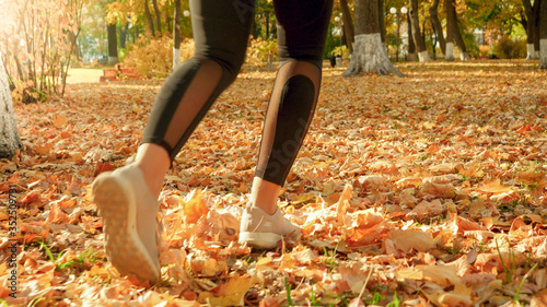 Closeup image of female feet running on fallen yellow tree leaves at autumn park
