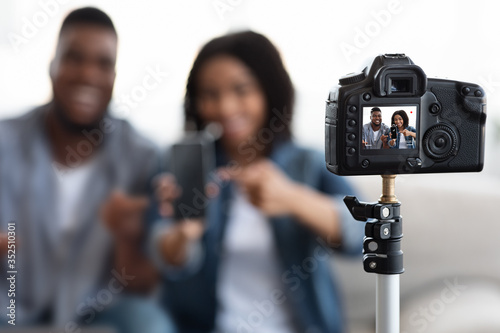 Camera recording video of cheerful african blogger couple presenting new smartphone