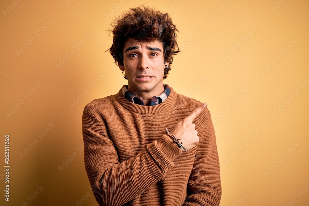 Young handsome man wearing casual shirt and sweater over isolated yellow background Pointing aside worried and nervous with forefinger, concerned and surprised expression Young handsome man wearing casual shirt and sweater over isolated yellow background Pointing aside worried and nervous with forefinger, concerned and surprised expression