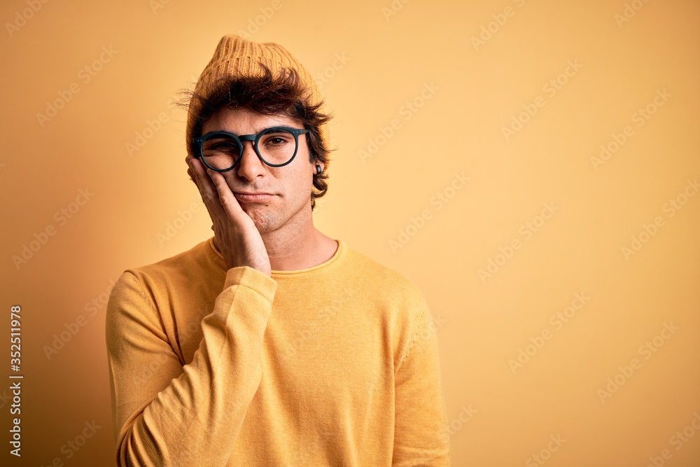 Young handsome man wearing casual t-shirt and glasses over isolated yellow background thinking looking tired and bored with depression problems with crossed arms. Young handsome man wearing casual t-shirt and glasses over isolated yellow background thinking looking tired and bored with depression problems with crossed arms.