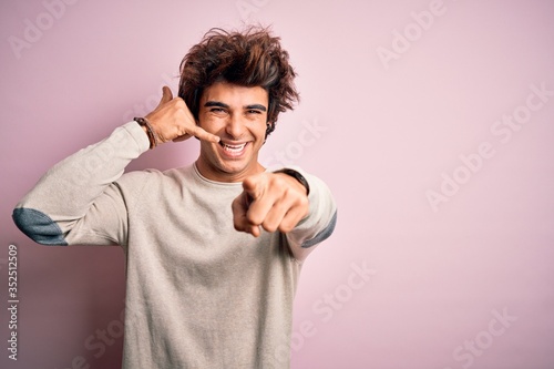 Young handsome man wearing casual t-shirt standing over isolated pink background smiling doing talking on the telephone gesture and pointing to you. Call me.
