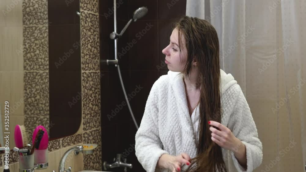 4K. Long shot. A girl / young woman, after a shower, puts oil on her hair with her hands. Girl smoothes her hair after a shower