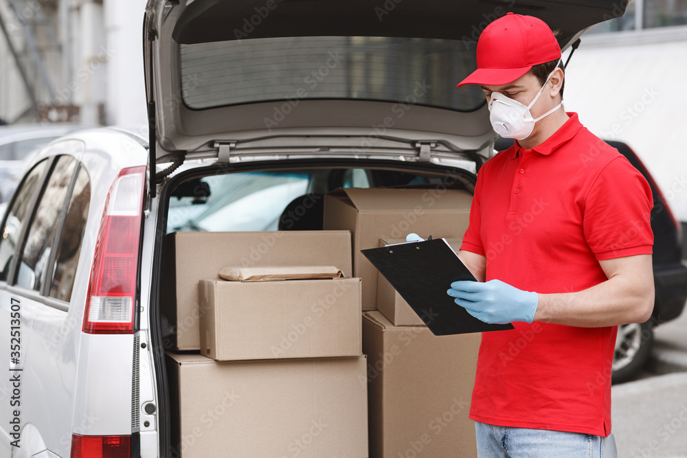 Transportation of parcels. Courier in protective mask and gloves checks parcel in tablet - obrazy, fototapety, plakaty 