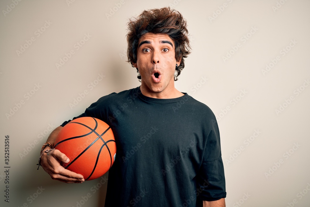 Young handsome sportsman holding basketball ball standing over isolated white background scared in shock with a surprise face, afraid and excited with fear expression Young handsome sportsman holding basketball ball standing over isolated white background scared in shock with a surprise face, afraid and excited with fear expression