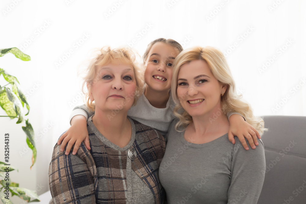 Three generations of women. Beautiful woman and teenage girl are kissing their granny while sitting on couch at home