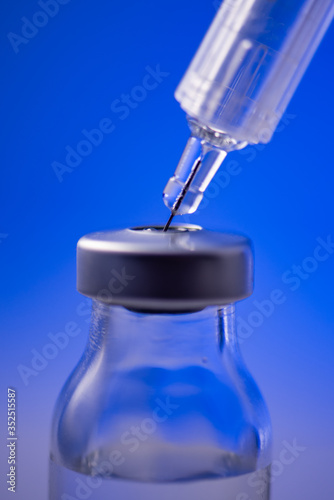 Photo of vaccine vial with syringe isolated over blue background. Medical concept shows a medical test tube and vaccines against coronavirus. Copy space