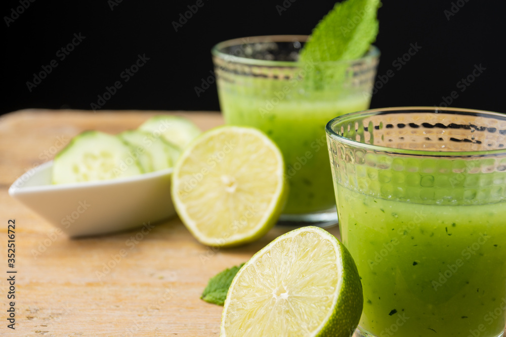 Close-up of two glasses with cucumber juice, cut limes, mint and cucumber slices, with selective focus, on wooden table, black background, horizontal Close-up of two glasses with cucumber juice, cut limes, mint and cucumber slices, with selective focus, on wooden table, black background, horizontal