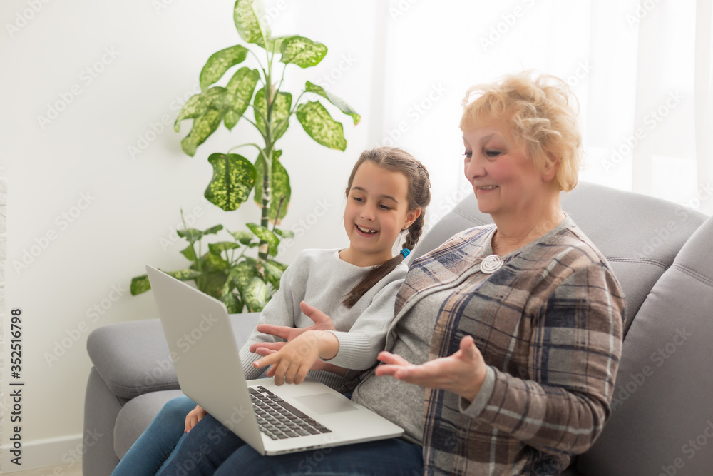 Side view of a grandmother and granddaughter using laptop in living room at home Side view of a grandmother and granddaughter using laptop in living room at home