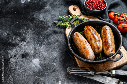 Tasty homemade sausages in a skillet. Pork, beef and chicken meat. Black background. Top view. Copy space