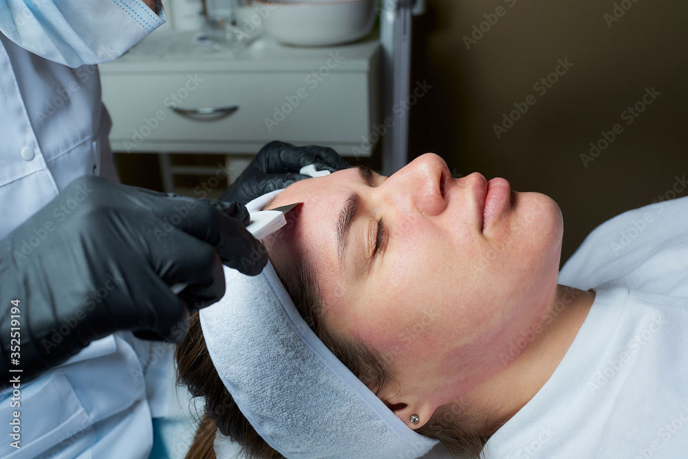 A close-up photo of the girl's face after a warming lotion during an ultrasonic procedure in the cosmetology office. A cosmetologist in disposable gloves peeling face with an ultrasonic skin scrubber.