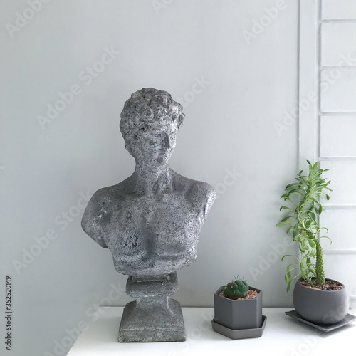 A half body of human stucco sculpture and cactus plant in concrete pots on white table.