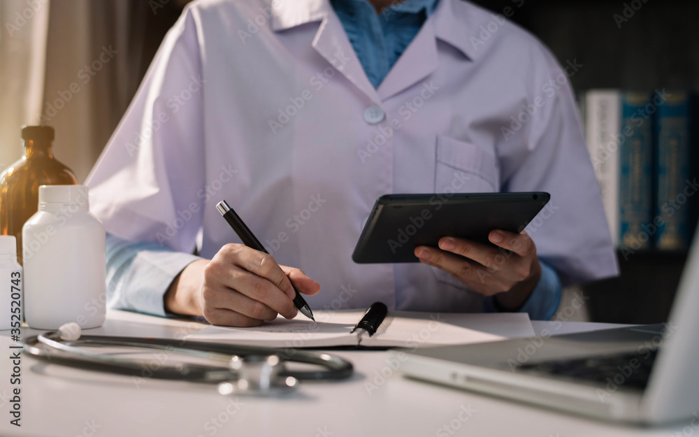 Doctor working on laptop computer, writing prescription clipboard with record information paper folders on desk in clinic, Healthcare and medical concept. Doctor working on laptop computer, writing prescription clipboard with record information paper folders on desk in clinic, Healthcare and medical concept.