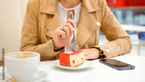 Closeup image of young woman eating sweet cake with fork in cafe
