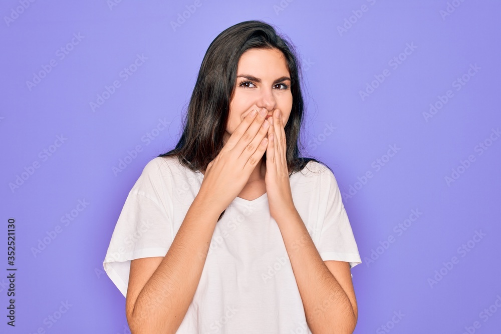 Young beautiful brunette woman wearing casual white t-shirt over purple background laughing and embarrassed giggle covering mouth with hands, gossip and scandal concept Young beautiful brunette woman wearing casual white t-shirt over purple background laughing and embarrassed giggle covering mouth with hands, gossip and scandal concept