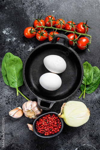 Concept of cooking Breakfast with fried or boiled eggs. Ingredients Eggs, onion, garlic, tomatoes, pepper, spinach. Black background. Top view