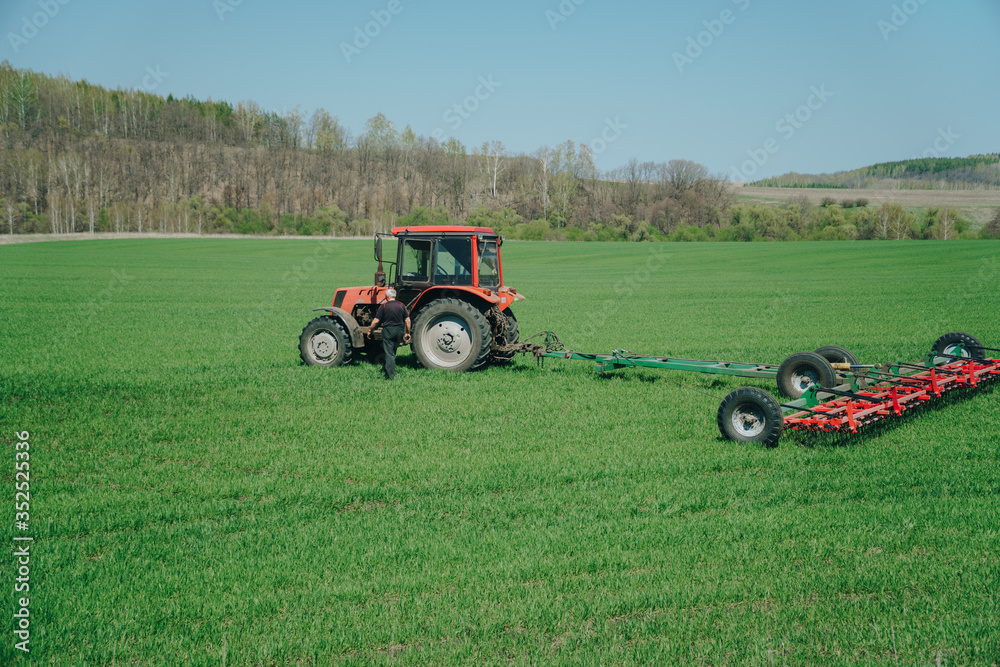 The tractor is working on a green spring field. Agriculture with cereal crops The tractor is working on a green spring field. Agriculture with cereal crops