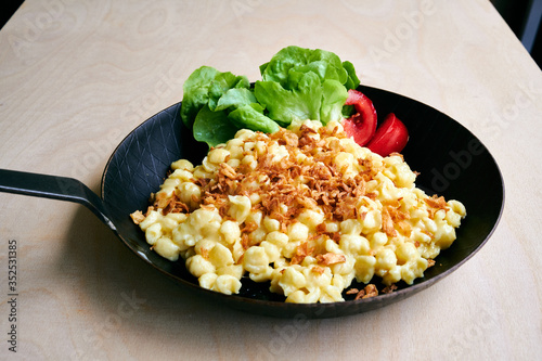 Bayrische Käsepätzle Kasspatzen mit Röstzwiebeln in einer Eisenpfanne auf einem Holztisch photo