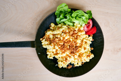 Bayrische Käsepätzle Kasspatzen mit Röstzwiebeln in einer Eisenpfanne auf einem Holztisch photo