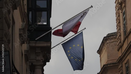 National flag of Malta and the European Union on the Central street of Valletta. 
Handheld shot.