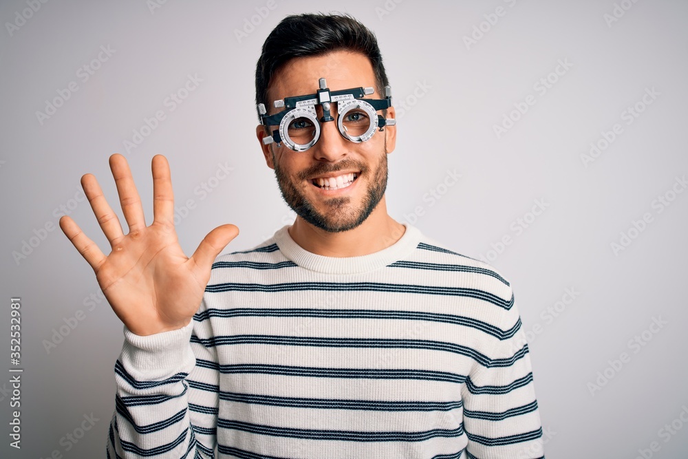 Young handsome man with beard wearing optometry glasses over isolated white background showing and pointing up with fingers number five while smiling confident and happy.