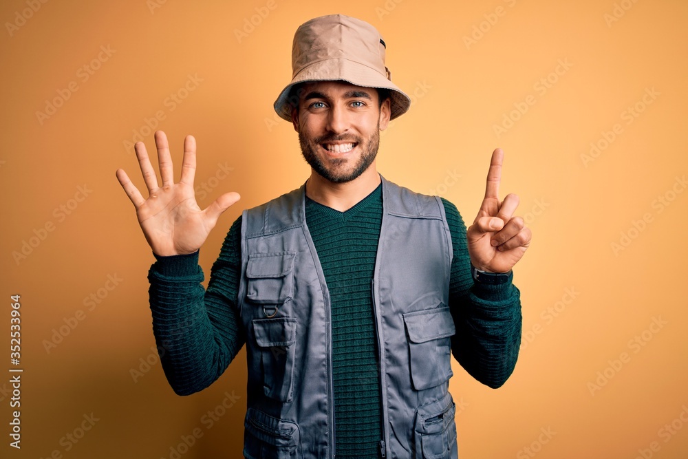 Handsome tourist man with beard on vacation wearing explorer hat over yellow background showing and pointing up with fingers number six while smiling confident and happy. Handsome tourist man with beard on vacation wearing explorer hat over yellow background showing and pointing up with fingers number six while smiling confident and happy.