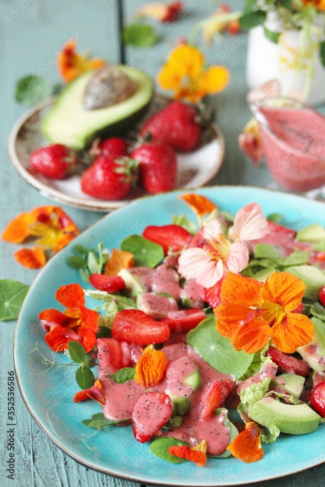 salad with nasturtium flowers and leaves with strawberries and avocados. dressed with strawberry vinaigrette or strawberry dressing with poppy seeds. bright summer salad with edible flowers. 