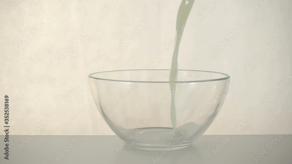 Milk is poured and splashed in slow motion into a transparent bowl on a white background. Milk is poured and splashed in slow motion into a transparent bowl on a white background.