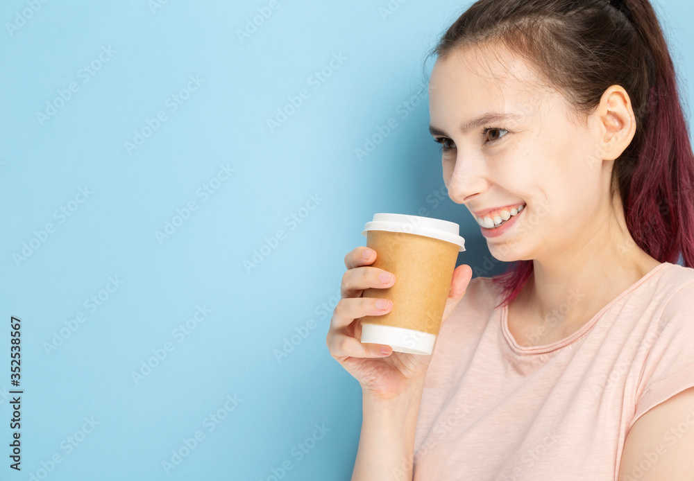 Young woman drinks coffee from paper cup and smiles on blue background. Copy space Young woman drinks coffee from paper cup and smiles on blue background. Copy space
