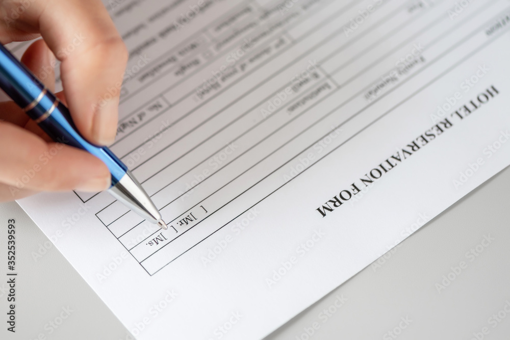 Woman filling hotel reservation form putting check mark on Mrs. Reception desk. Hotel service, registration. Close up. Selective focus. Woman filling hotel reservation form putting check mark on Mrs. Reception desk. Hotel service, registration. Close up. Selective focus.