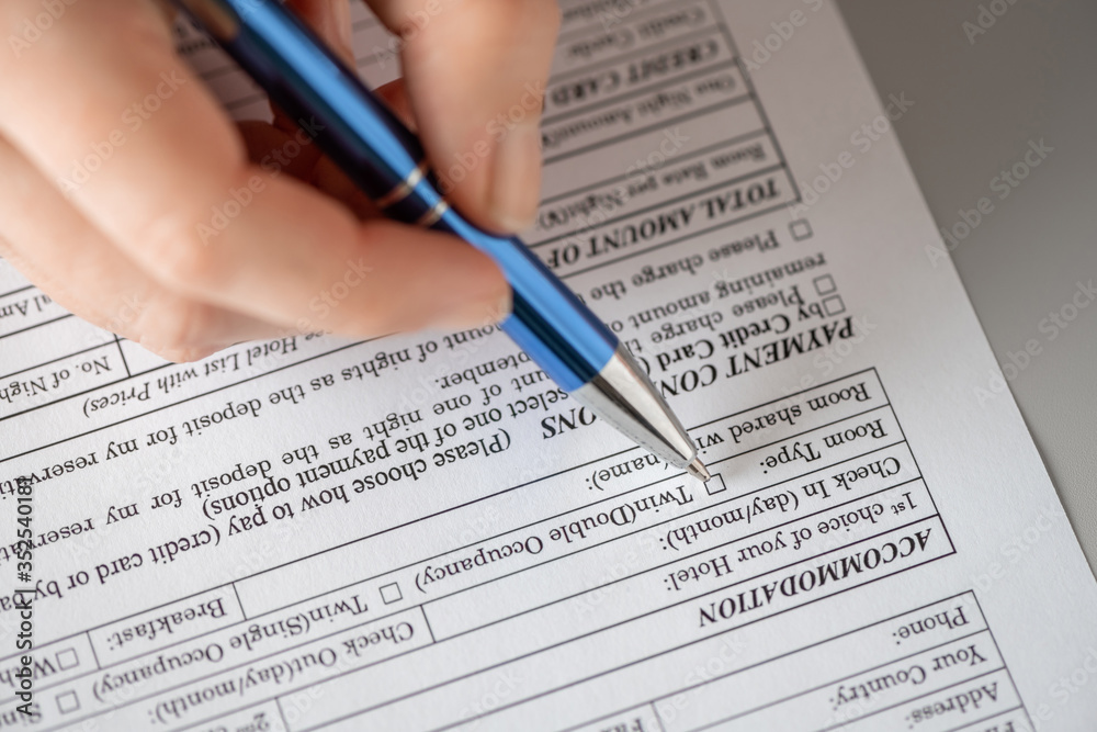 Woman filling hotel reservation form putting check mark on room type. Reception desk. Hotel service, registration. Close up. Selective focus. Woman filling hotel reservation form putting check mark on room type. Reception desk. Hotel service, registration. Close up. Selective focus.
